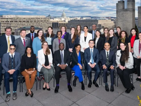 A group of people in professional attire smile at the camera with white brick buildings in the background.