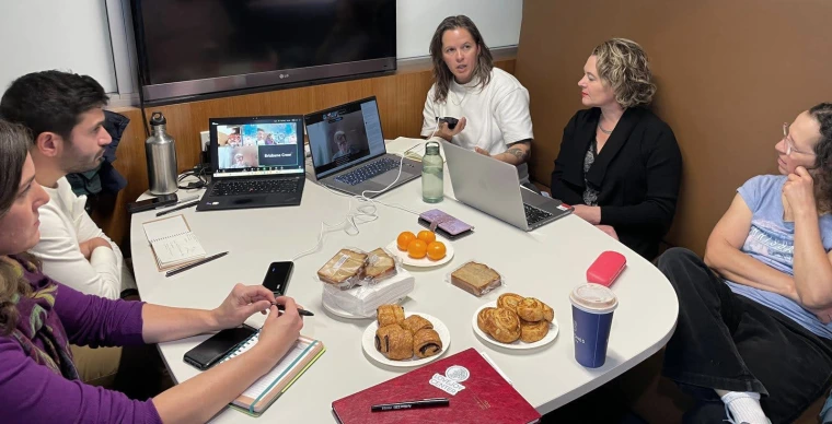 People grouped around a table with laptops and snacks.