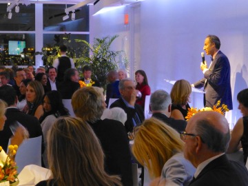 A man speaks in front of a group assembled for dinner.