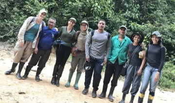 A group of people standing shoulder to shoulder with the rainforest behind them.