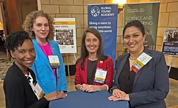 A group of women in conference attire stand smiling around a table.